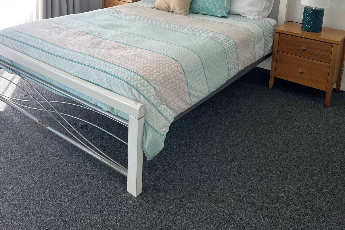 Une chambre à coucher bien rangée, avec un lit, deux tables de chevet, un ventilateur de plafond et un tableau encadré au mur.