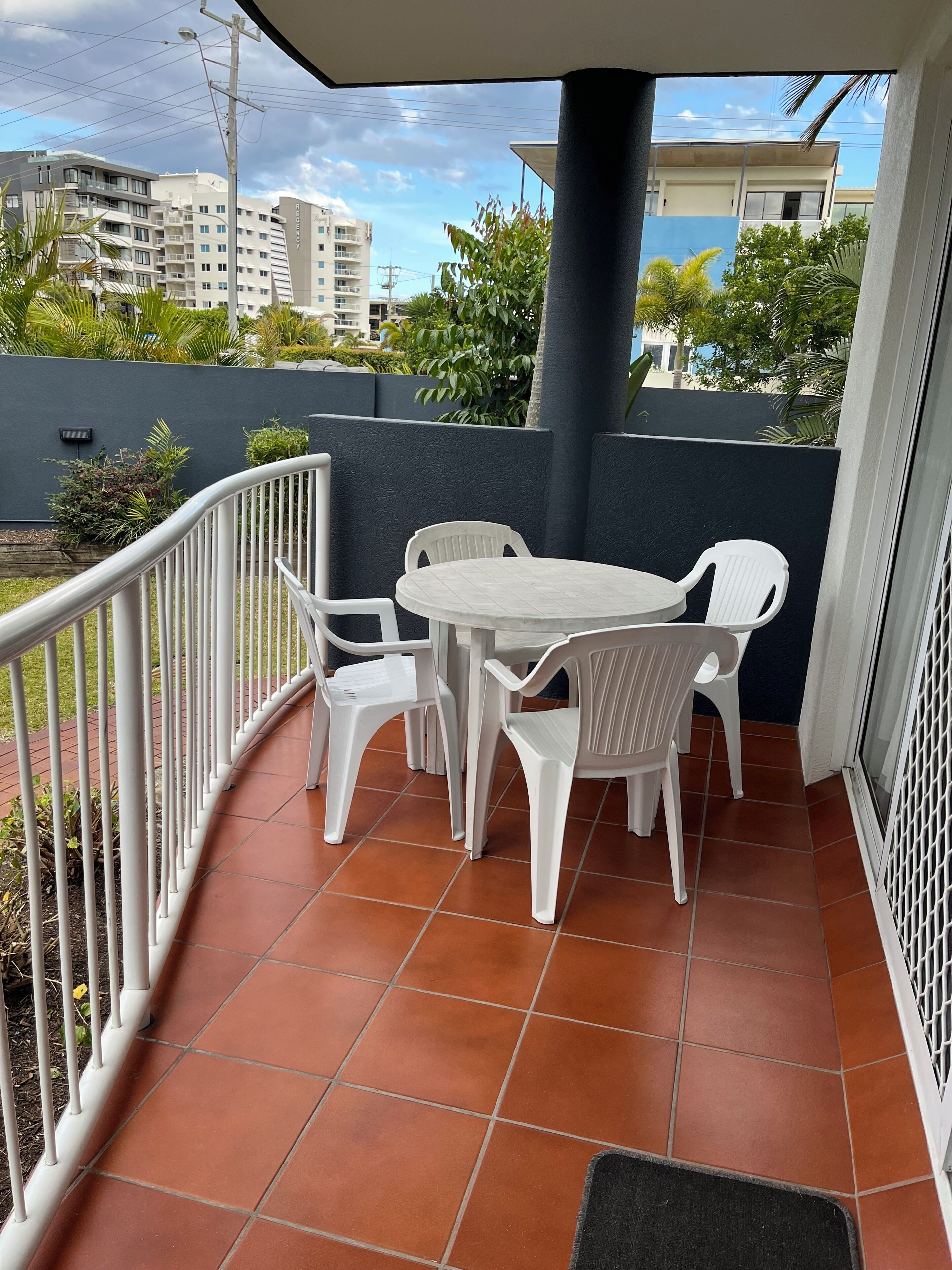 A balcony with a round table and four chairs, surrounded by a white railing.