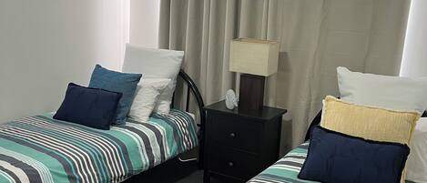 A room with two single beds, a ceiling fan, a framed picture on the wall, and a nightstand with a lamp.