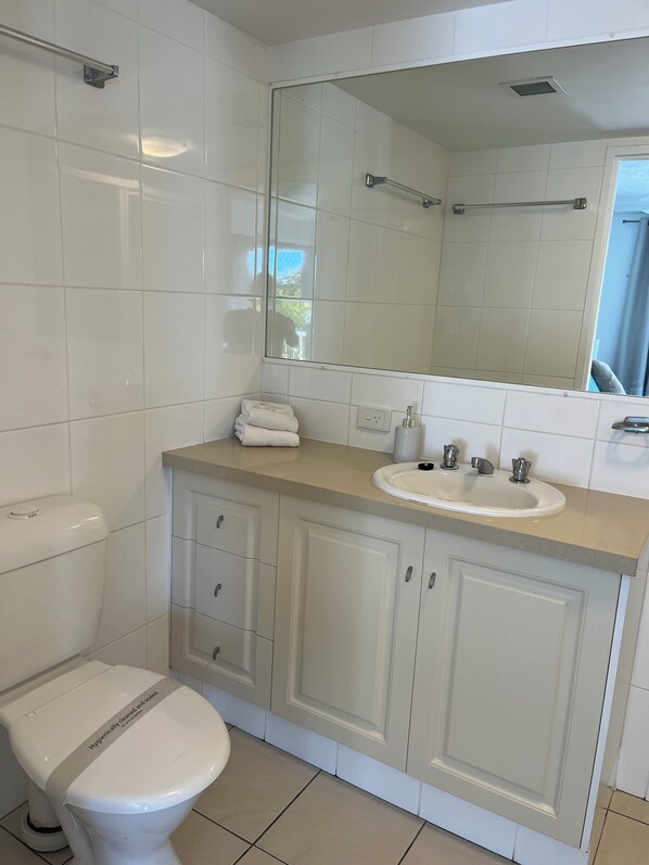 A bathroom with a toilet, sink, mirror, and cabinets.