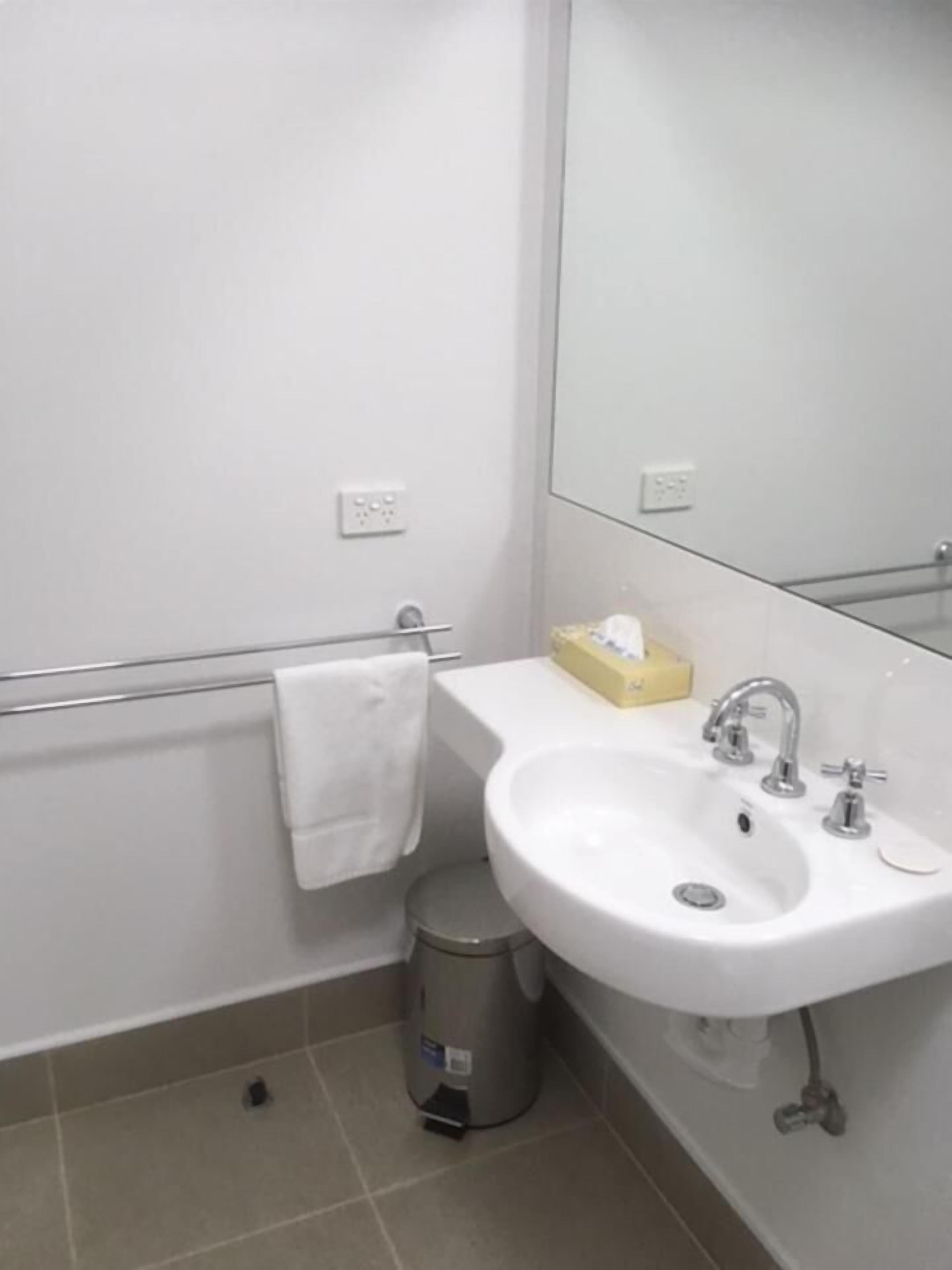 A bathroom with a white sink, a mirror, and a trash can.