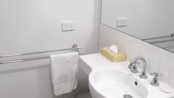A bathroom with a white sink, a mirror, and a trash can.