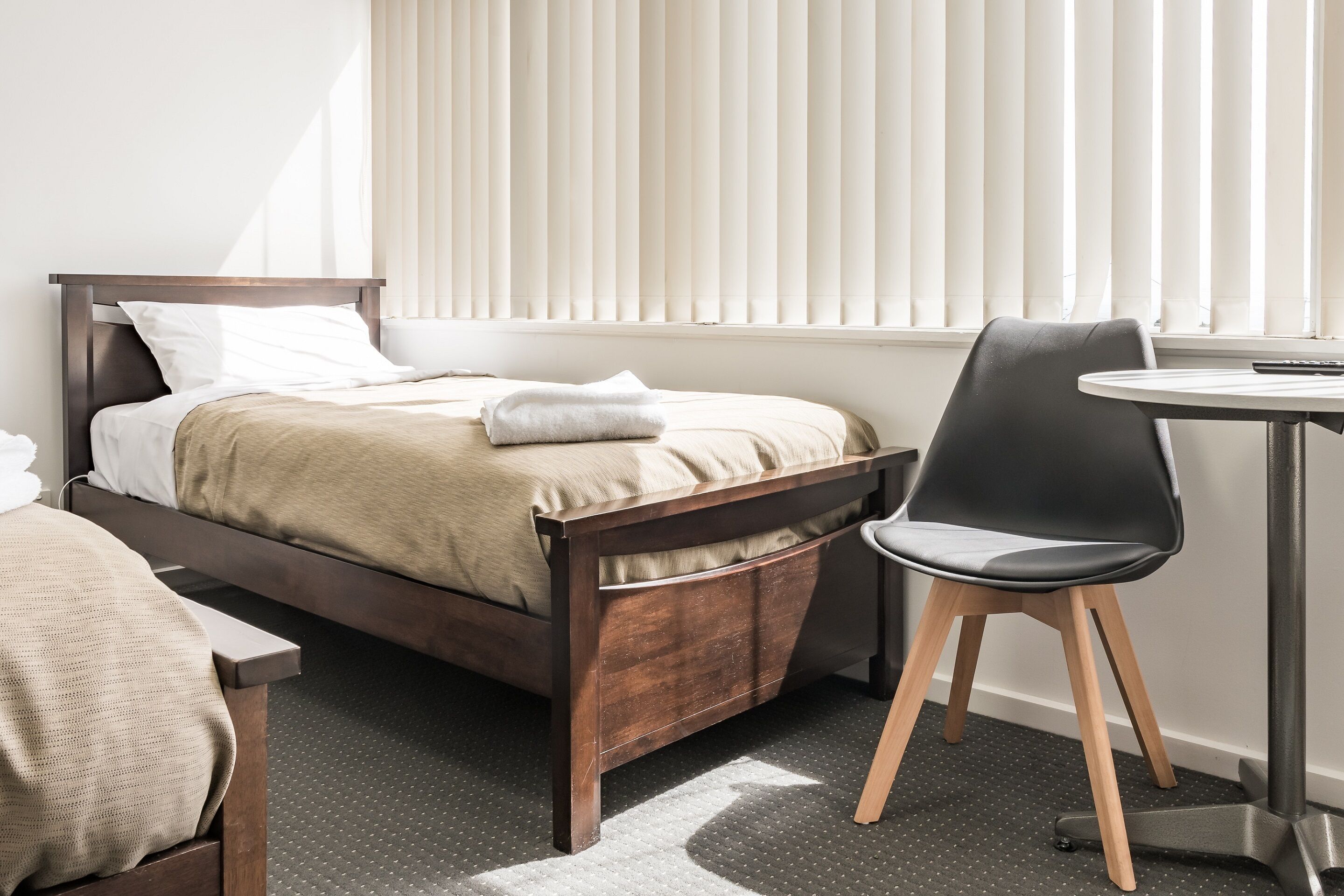 A bedroom with a bed, a chair, a small table, and a window with blinds.