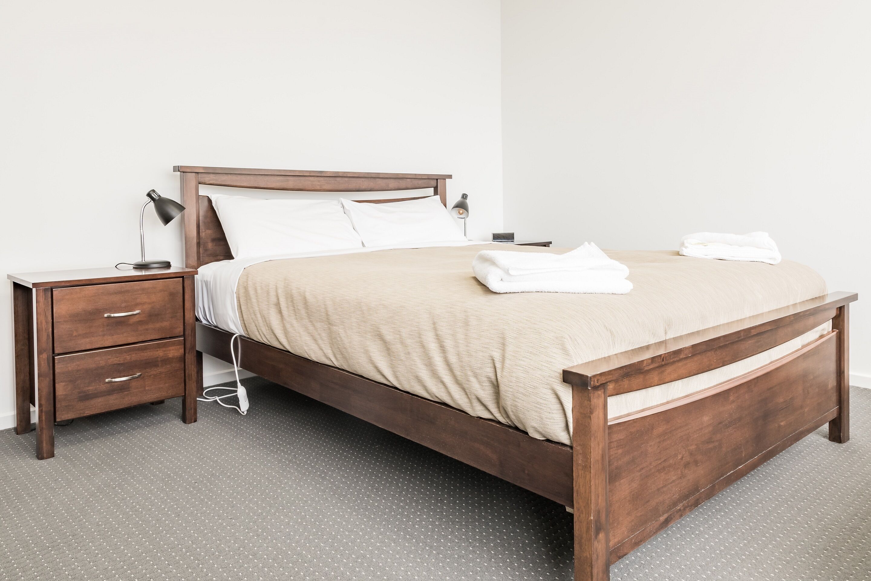 A neatly made bed with a wooden frame, a bedside table with a lamp, and a drawer unit.