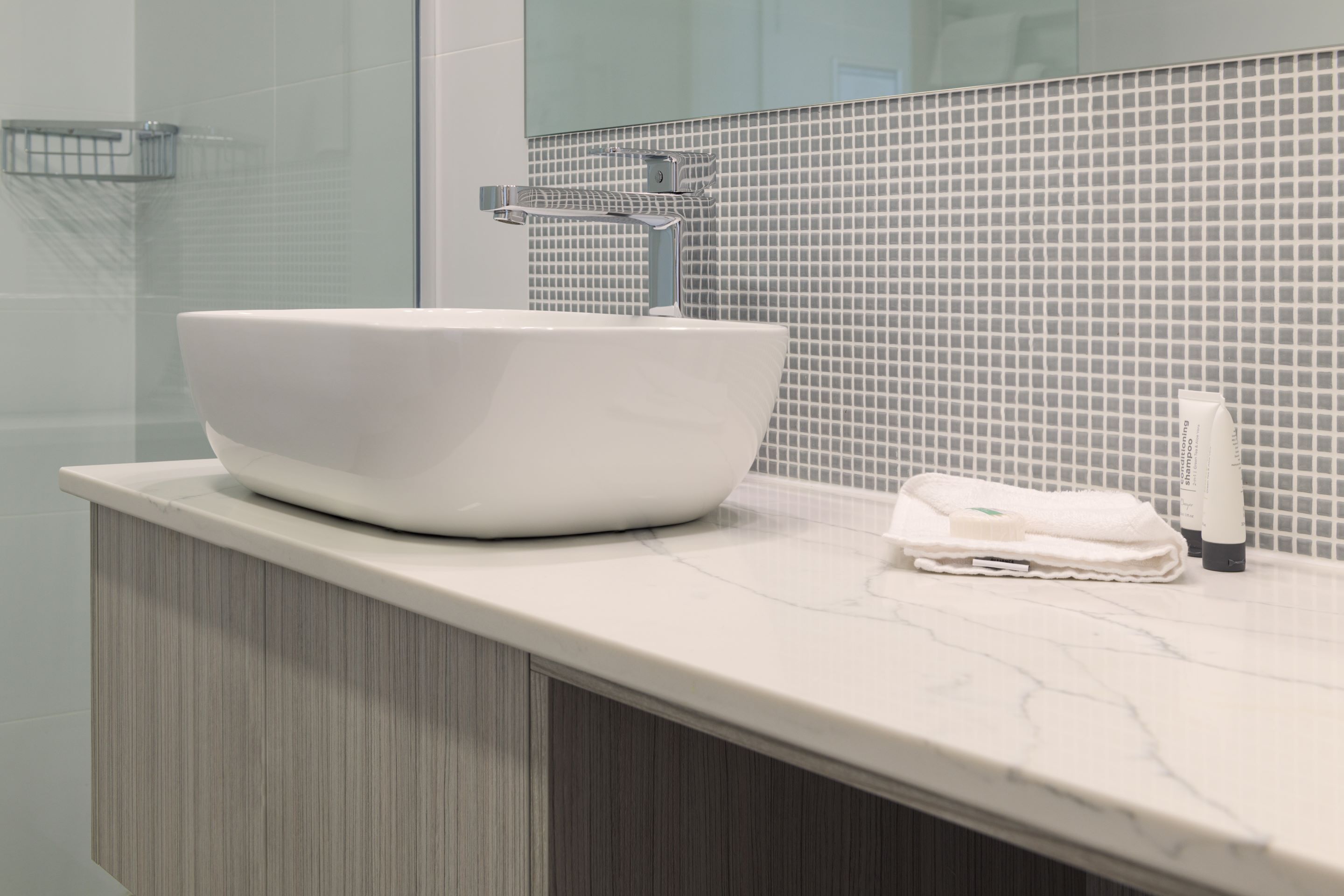 Un baño moderno con un lavamanos blanco de diseño, una cabina de ducha con paredes de vidrio y un salpicadero de azulejos.