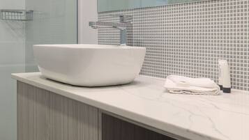 Un baño moderno con un lavamanos blanco de diseño, una cabina de ducha con paredes de vidrio y un salpicadero de azulejos.