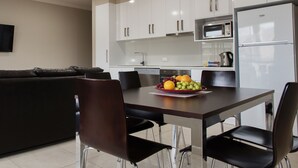 Una cocina moderna con armarios blancos, una mesa de comedor con sillas, un sofá de cuero negro y un frutero sobre la mesa.