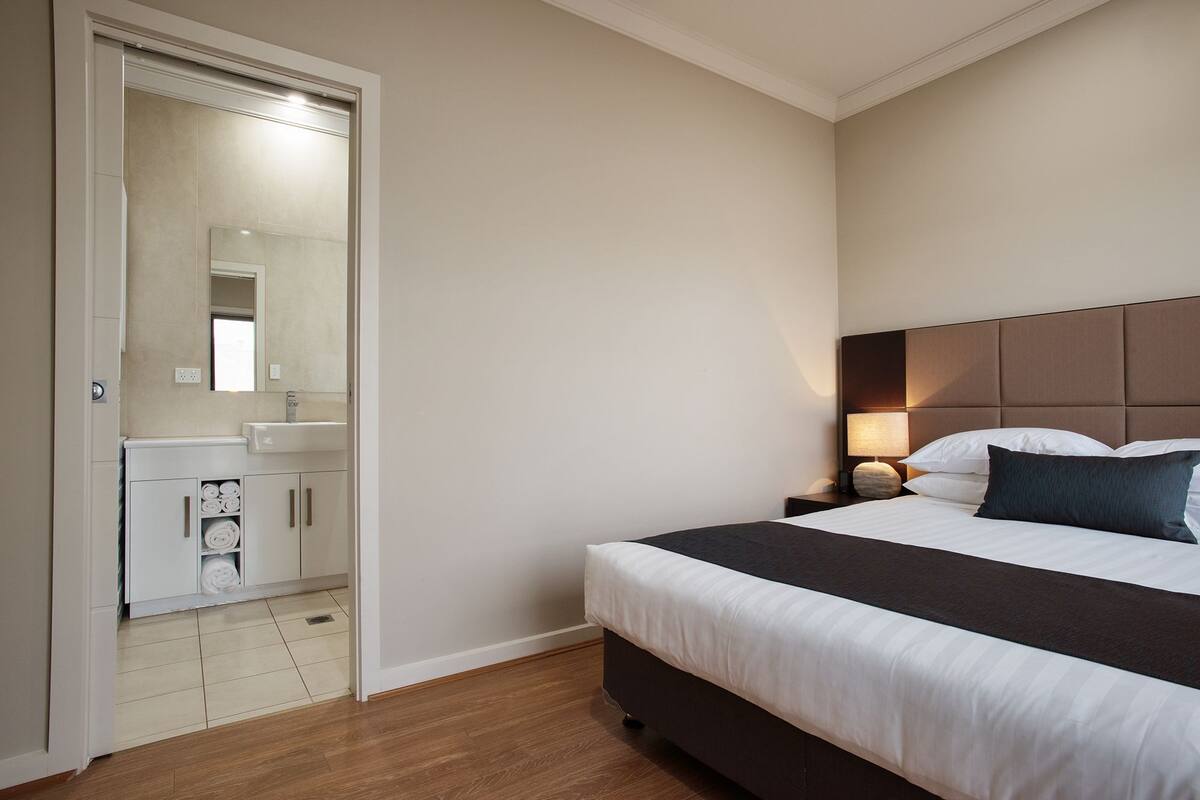 A hotel room with a bed, bedside table, lamp, and a bathroom with a mirror and sink.