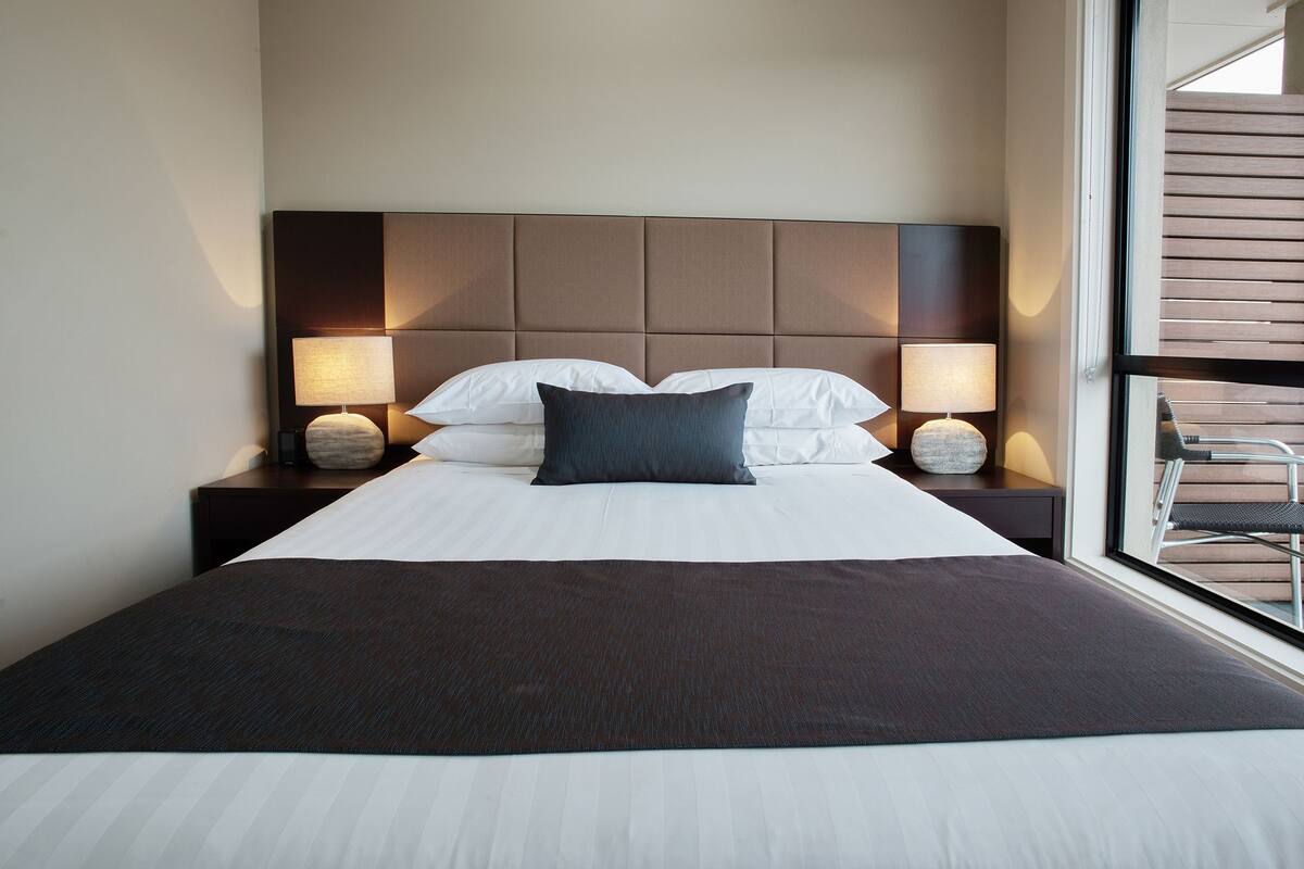 A neatly made bed with white linens and a dark throw blanket, flanked by two bedside tables with lamps.