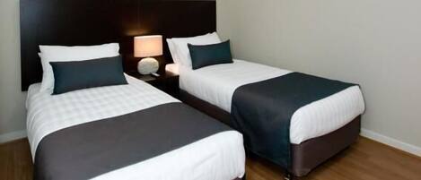 A hotel room with two beds, a nightstand, a lamp, and an air conditioning unit.