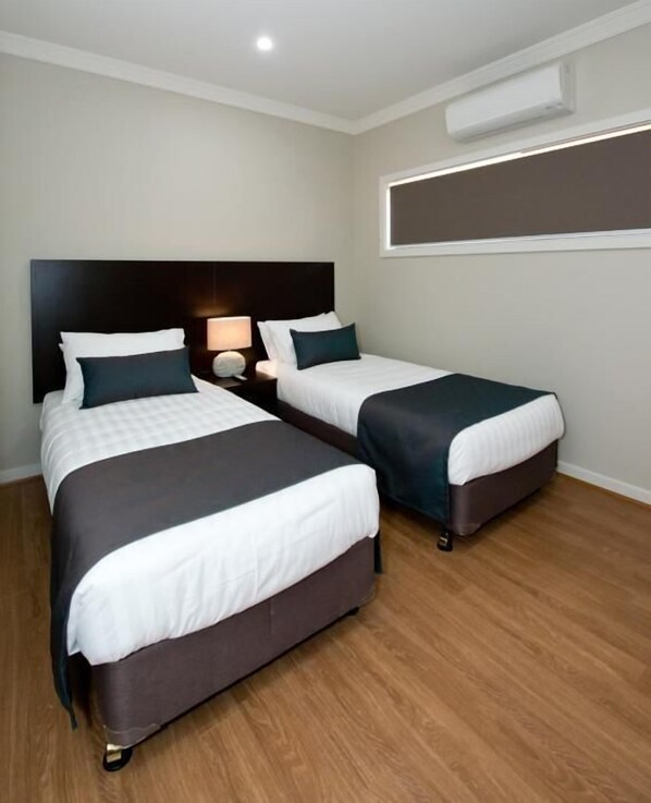 A hotel room with two beds, a nightstand, a lamp, and an air conditioning unit.