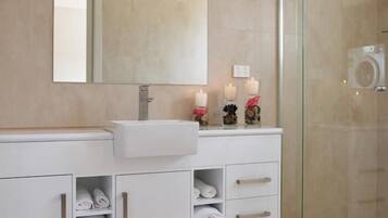 Un baño moderno con tocador blanco, un espejo grande y cabina de ducha de vidrio.