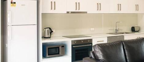A modern kitchen with white cabinets, a refrigerator, a stove, an oven, a microwave, and a coffee maker.