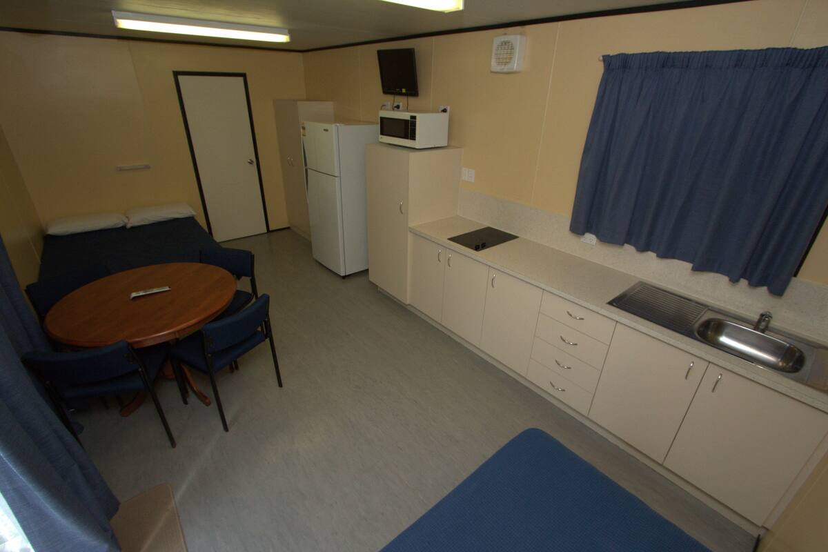 Una kitchenette compacta con microondas, refrigerador, lavamanos y un pequeño comedor con mesa y sillas.