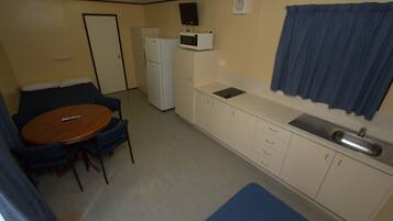 A compact kitchenette with a microwave, refrigerator, sink, and a small dining area with a table and chairs.