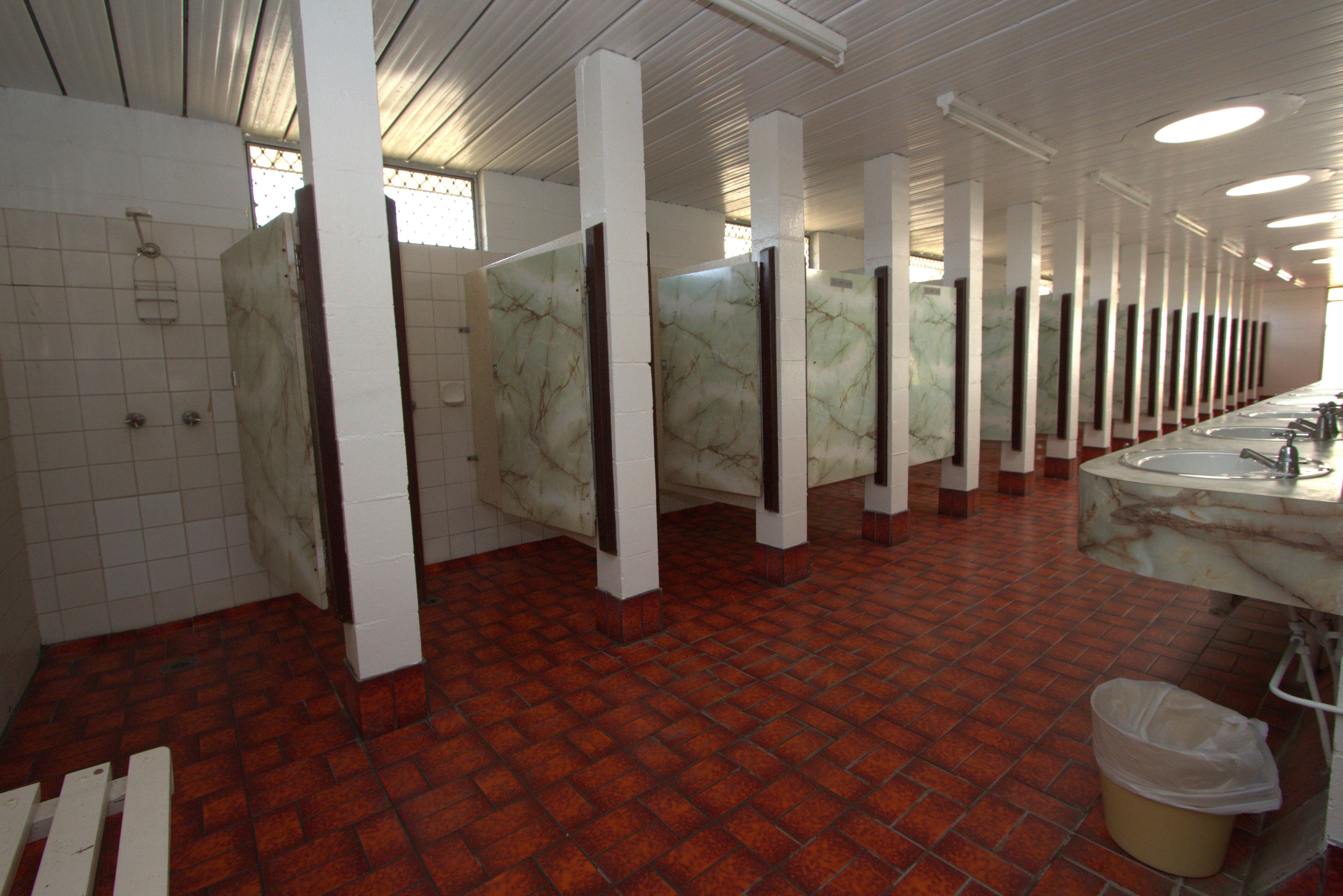Baño público con separadores de mármol, suelo de baldosas y zona de lavamanos.