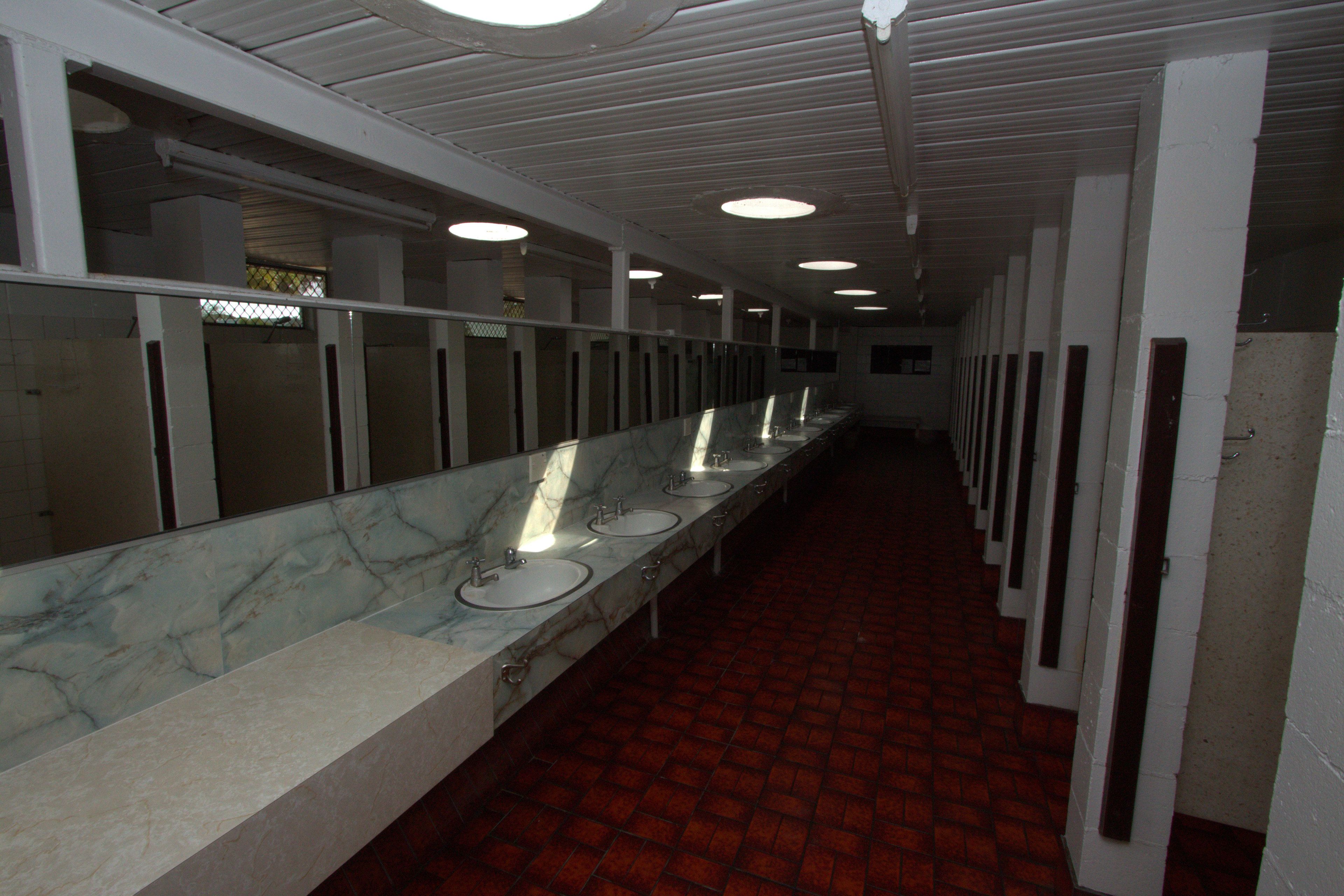 A long corridor with multiple sinks and mirrors, lined with white pillars and red-tiled flooring.