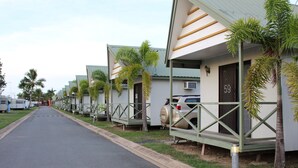 A row of mobile homes with numbered doors, a paved road, and parked cars. - Central Tourist Park (North Mackay)