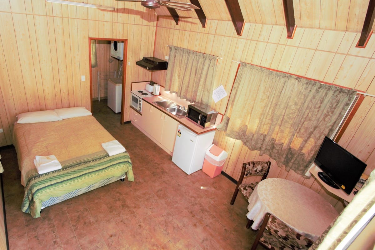 Una habitación de hotel pequeña con una cama individual, una kitchenette y una televisión, además de una silla.