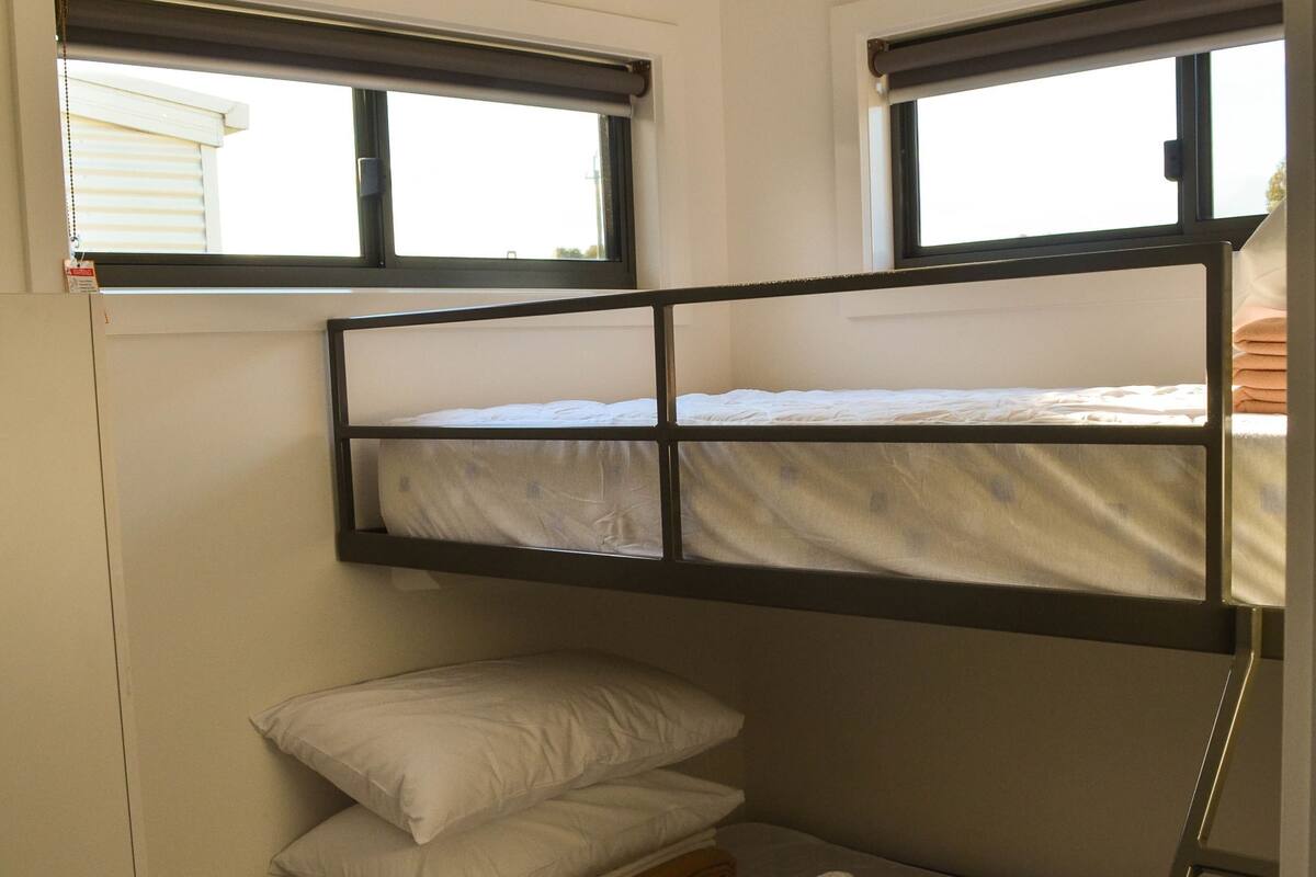 Quarto com beliche, janela, uma mesinha e prateleira fixa na parede.