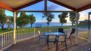 Un espace extérieur abrité, doté d’une table et de chaises, qui offre une vue sur une étendue d’eau et des arbres.