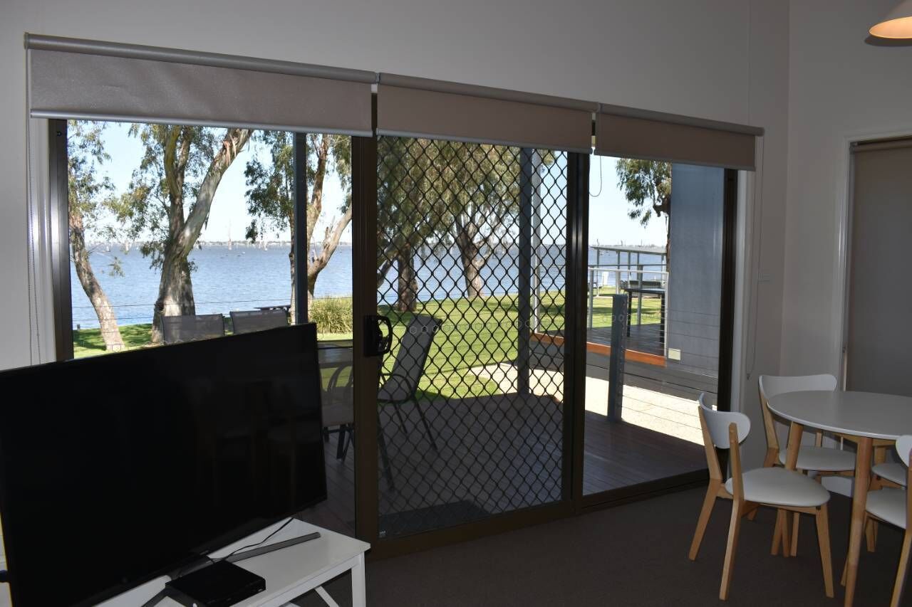 A room with a TV, a table with chairs, and a view of a lake through a sliding door.