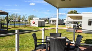 Un patio cubierto con mobiliario exterior, una piscina y vehículos recreativos al fondo.