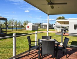 Un patio cubierto con mobiliario exterior, una piscina y vehículos recreativos al fondo.
