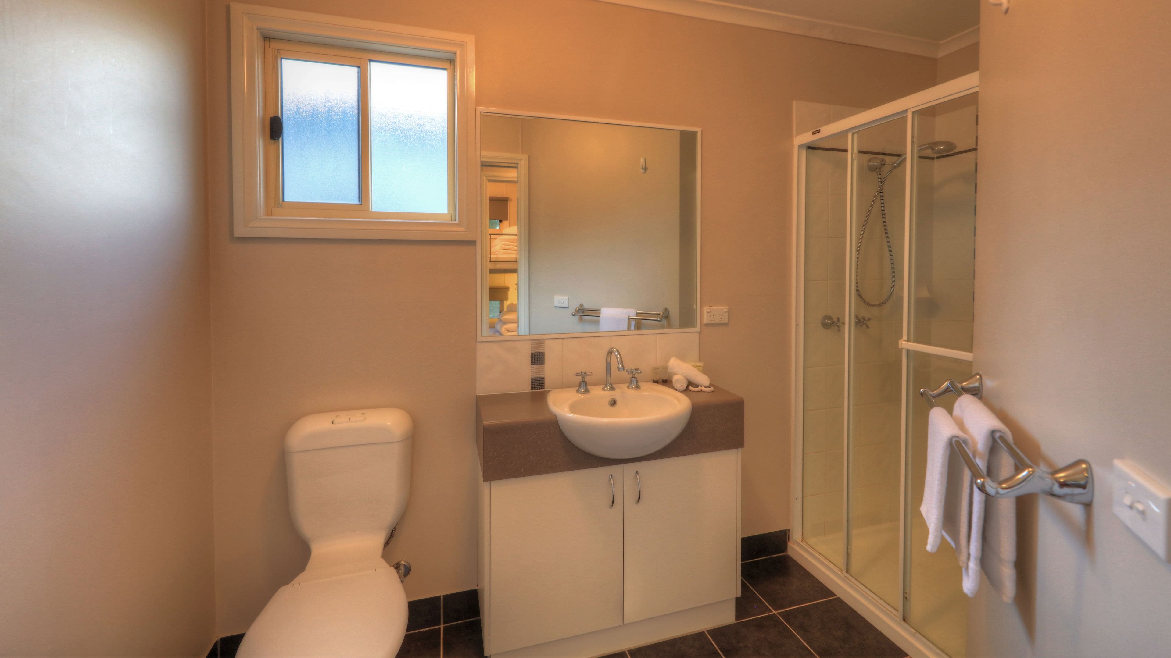 A bathroom with a toilet, sink, mirror, and glass-enclosed shower.