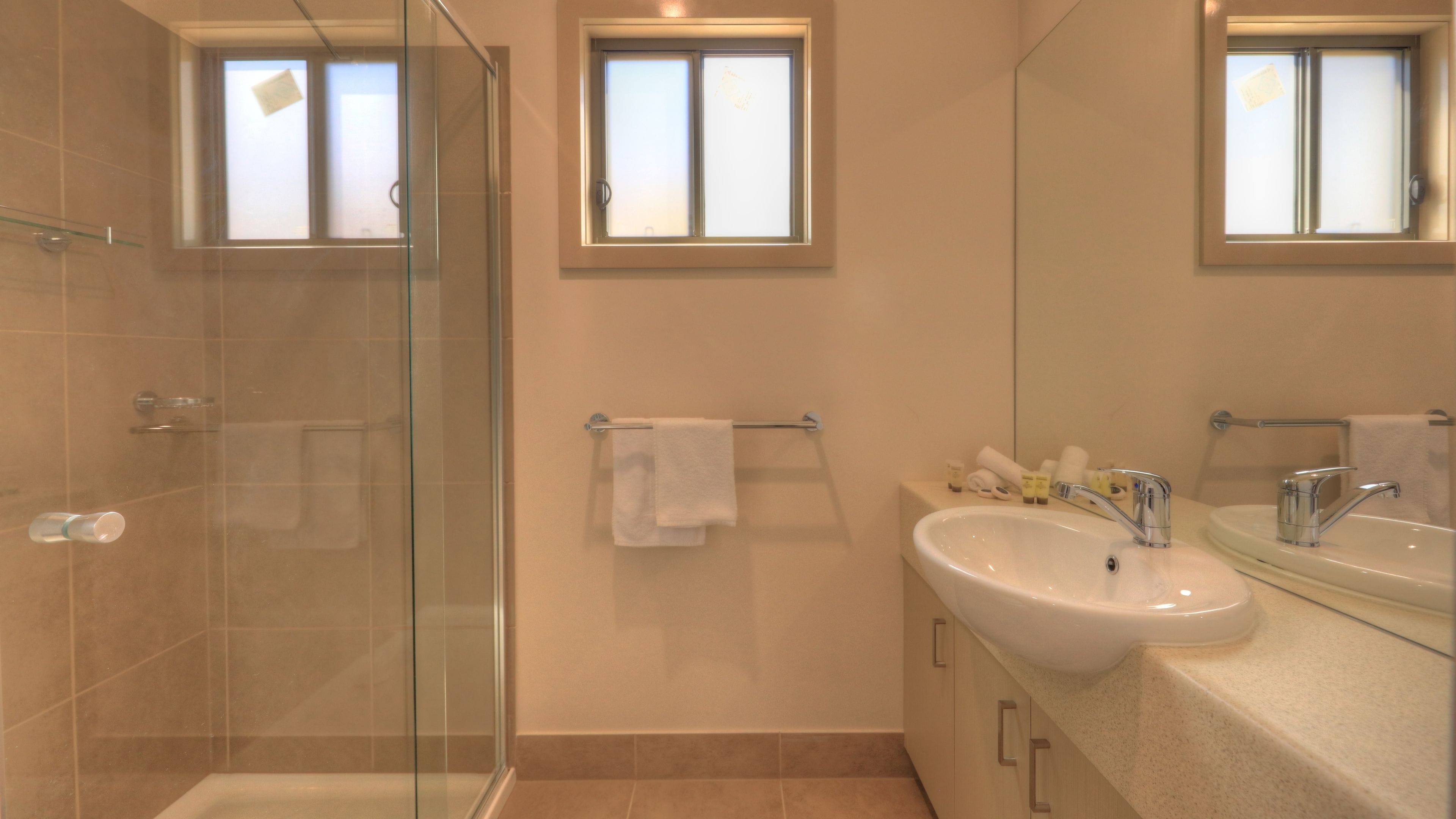 A modern bathroom with a glass shower enclosure, a sink with a mirror, and two towel racks.