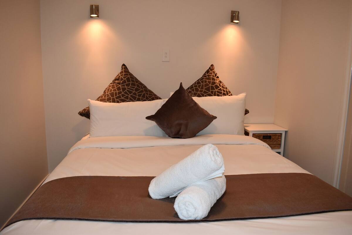 Uma cama bem arrumada com um cobre-leito marrom, duas almofadas com padrão de girafa e uma toalha dobrada sobre a cama.