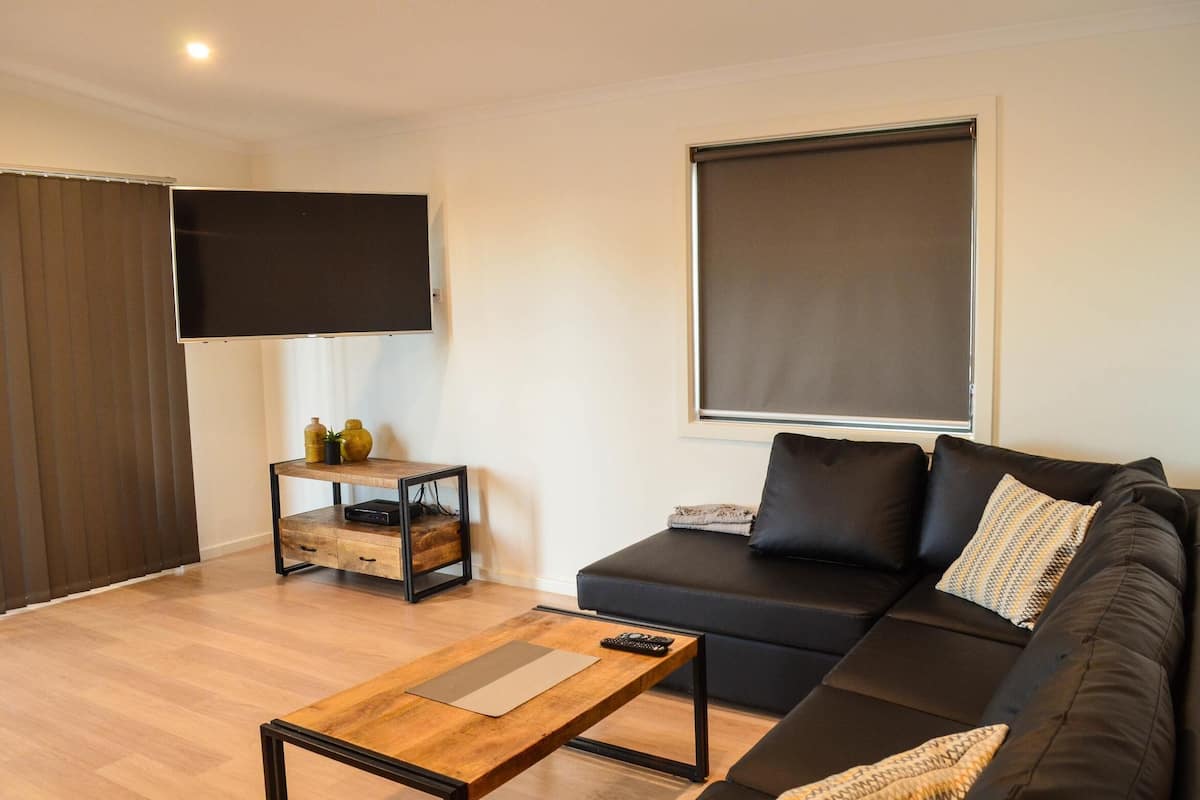 Uma sala de estar moderna com um sofá, uma mesa de centro, uma TV na parede e uma porta de correr.