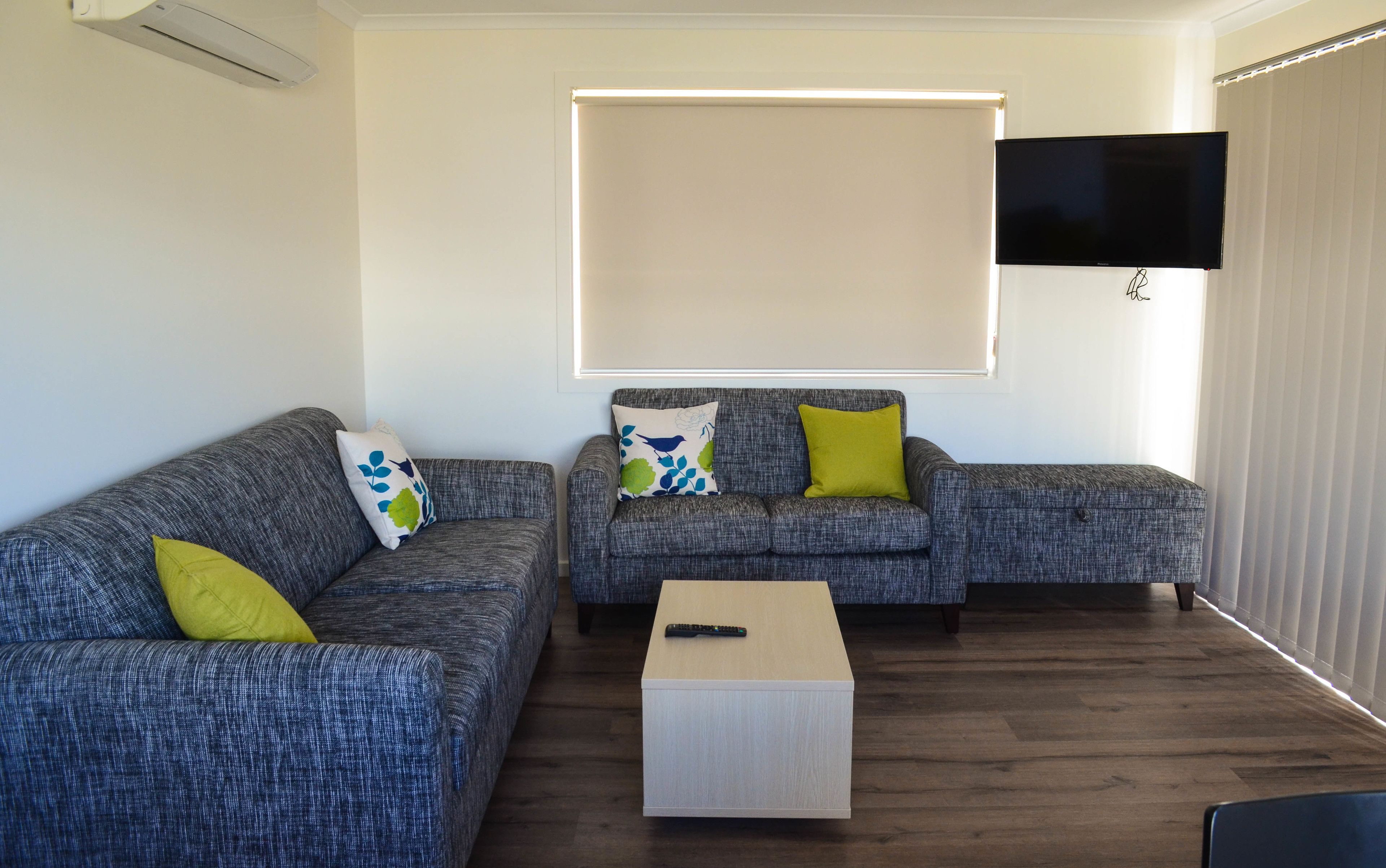 Uma sala de estar com dois sofás cinza, uma pequena mesa de centro de madeira e uma televisão de tela plana na parede.