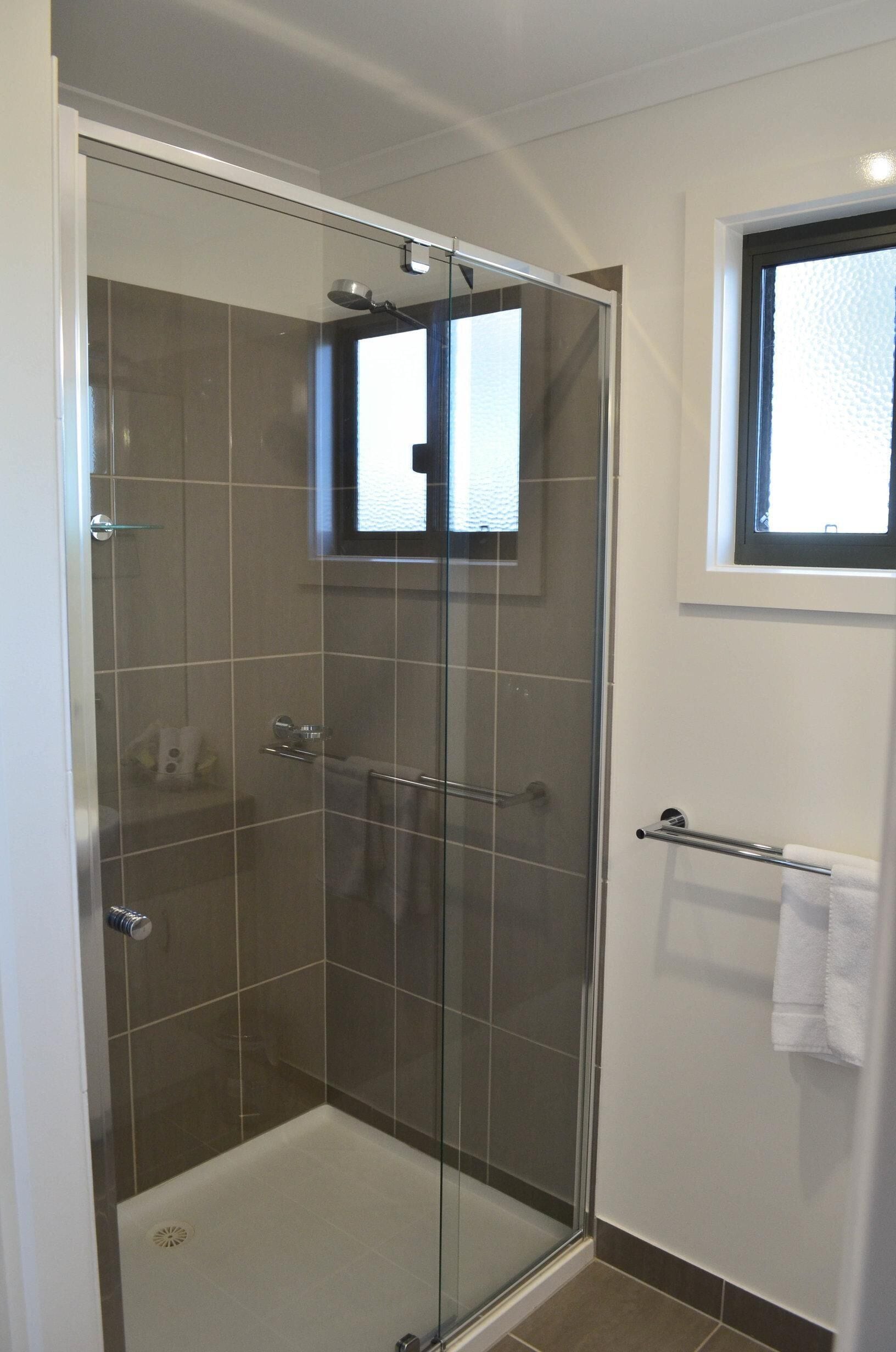 A glass-enclosed shower stall with a white tiled floor, a glass door, and a window above the shower.