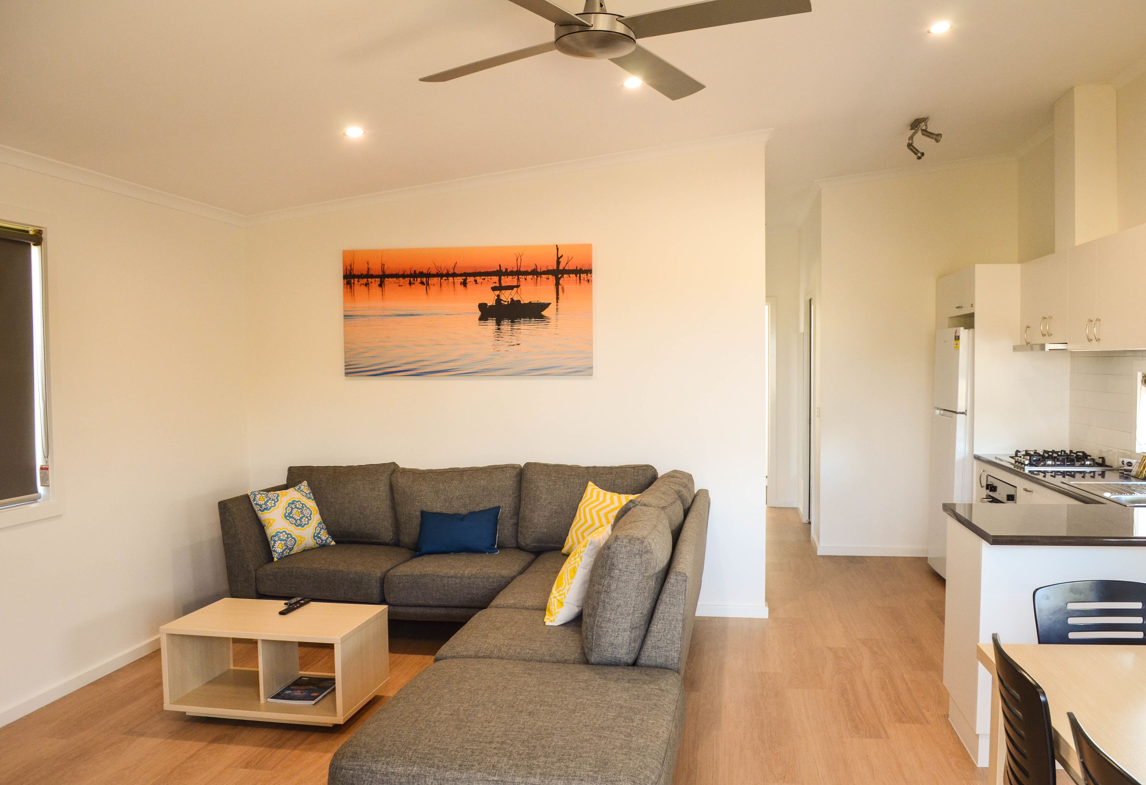 A modern living room with a sectional sofa, a coffee table, and a painting of a sunset over water.