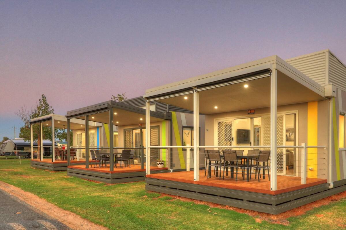 Alojamento moderno estilo motorhome com duas varandas cobertas, cada uma com assentos e mesas.