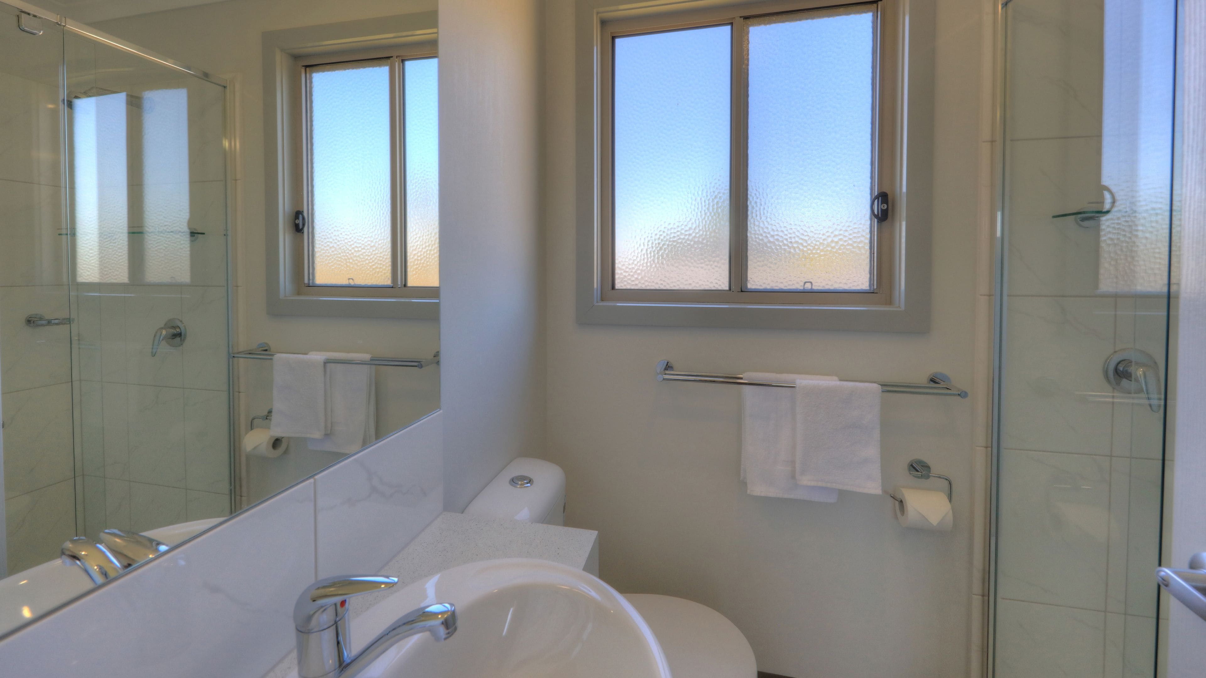 A bathroom with a glass shower enclosure, a bathtub, a toilet, and a window above the sink.