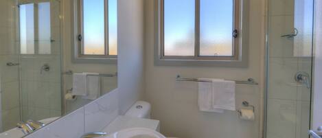 A bathroom with a glass shower enclosure, a bathtub, a toilet, and a window above the sink.