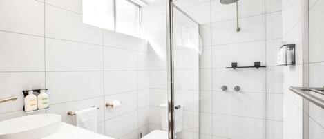 A modern bathroom with a glass shower enclosure, a white toilet, and a sink with toiletries.