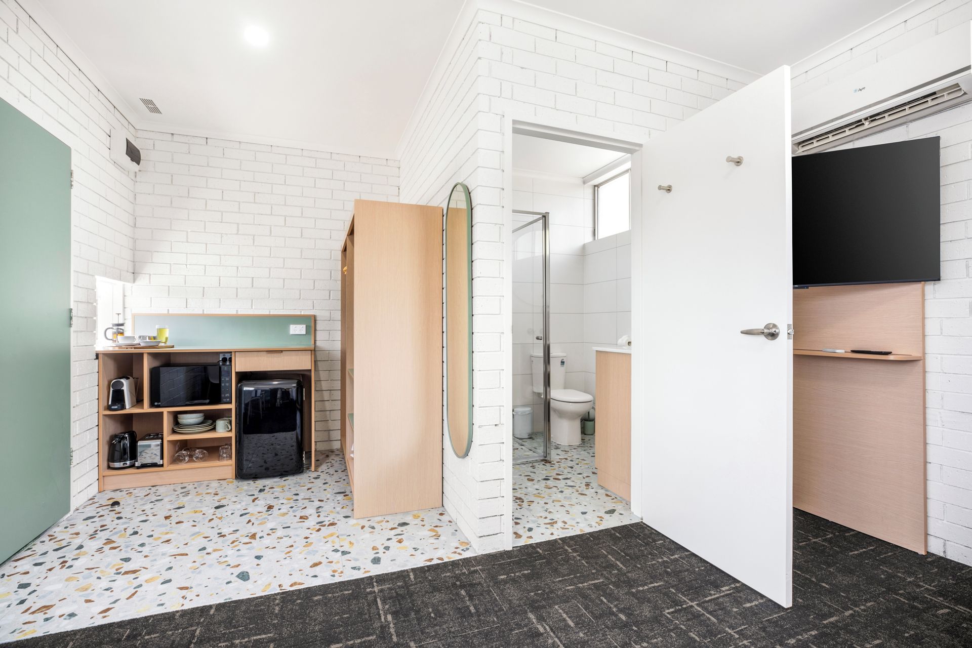 A compact kitchen with a microwave, kettle, and coffee maker on a white brick wall.