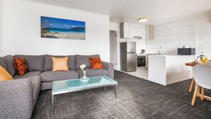 En moderne stue med en grå sofa, et glasbord og et maleri af en strand.