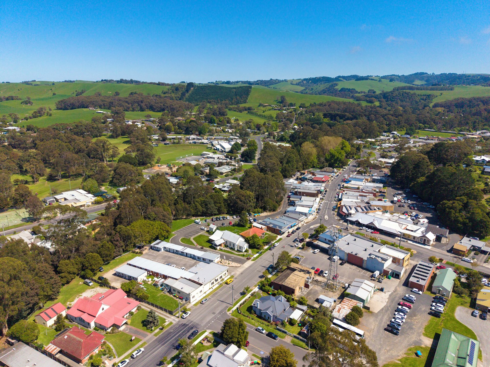 An aerial view of a town with a mix of residential and commercial buildings, roads, and green fields.