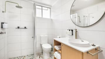 A modern bathroom with a glass shower enclosure, a toilet, a sink with a mirror, and a tiled floor.