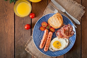 A breakfast plate with sausages, bacon, a fried egg, toast, and tomatoes on a wooden table. - Wilsons Promontory Motel (Foster)