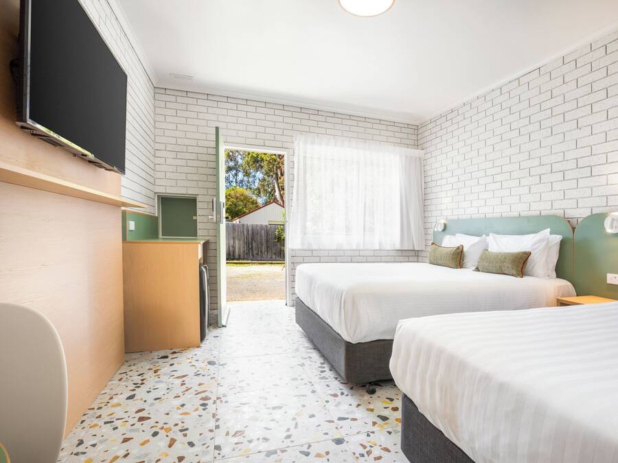 A hotel room with two beds, a TV, a desk, and a window with a view of the outside.