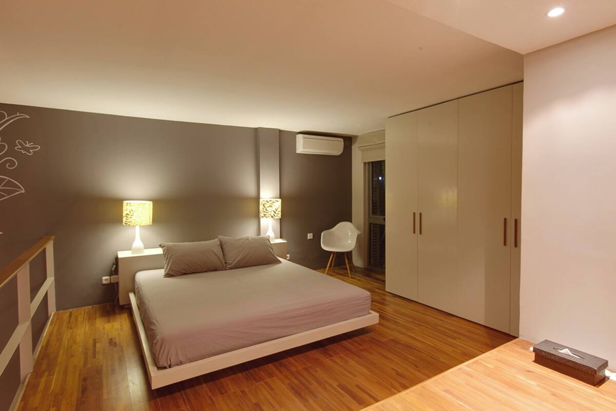 A modern bedroom with a bed, bedside lamps, a chair, and a wardrobe.