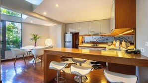 A modern kitchen with a central island, bar stools, and a dining area with a table and chairs. - Petitenget 501 (Keroboken Kelod)