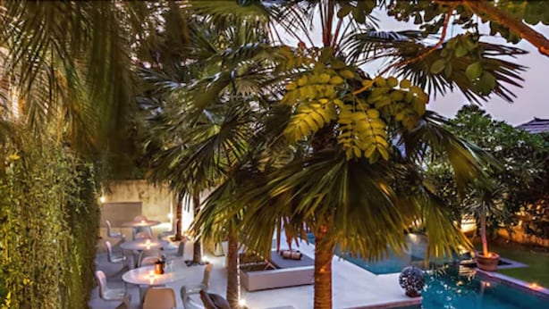 An outdoor pool area with lounge chairs and tables, surrounded by palm trees and greenery. - Petitenget 501 (Keroboken Kelod)