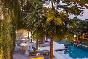 An outdoor pool area with lounge chairs and tables, surrounded by palm trees and greenery. - Petitenget 501 (Keroboken Kelod)