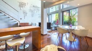 A modern interior with a wooden dining table, bar stools, and a word cloud wall. - Petitenget 501 (Keroboken Kelod)